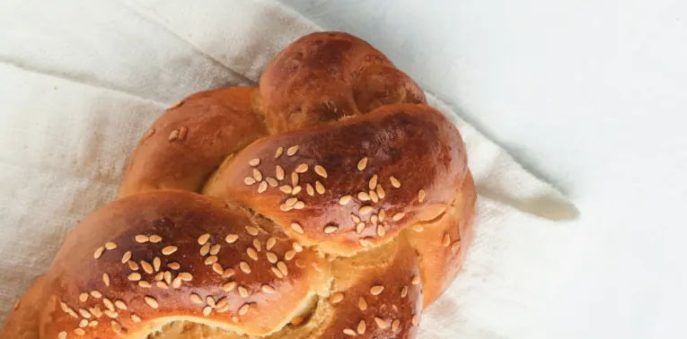 braided loaf of bread with sesame seeds laying on a white cloth