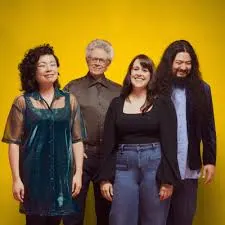 Four people stand against a yellow background.