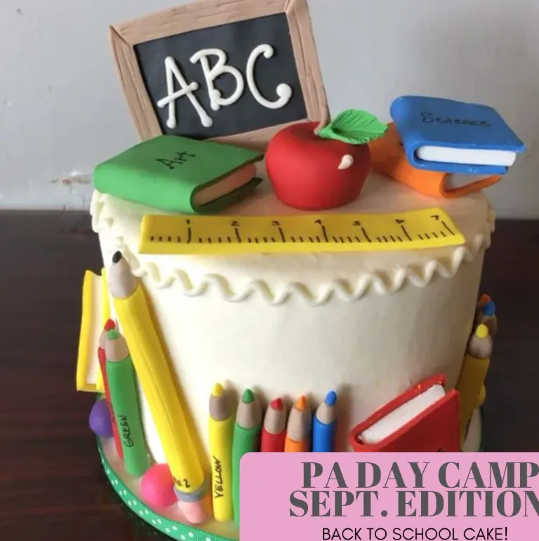 White cake decorated with fondant school supplies, like pencils and notebooks along the side, an apple on top with ruler