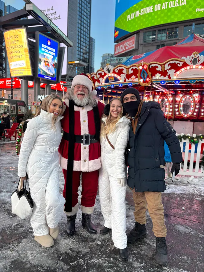 Santa Claus poses with three smiling adults dressed in winter coats at Toronto’s Holiday Fair in Sankofa Square.