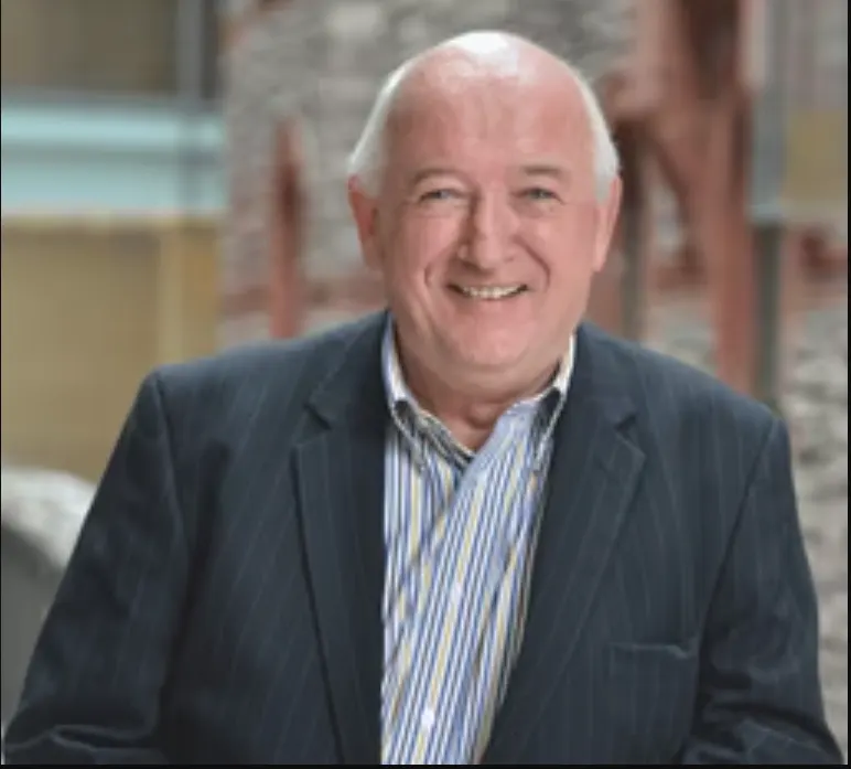 John O’Conor wears a suit and smiles.