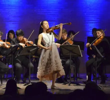 A group of young musicians on a stage. The background is illuminated blue.